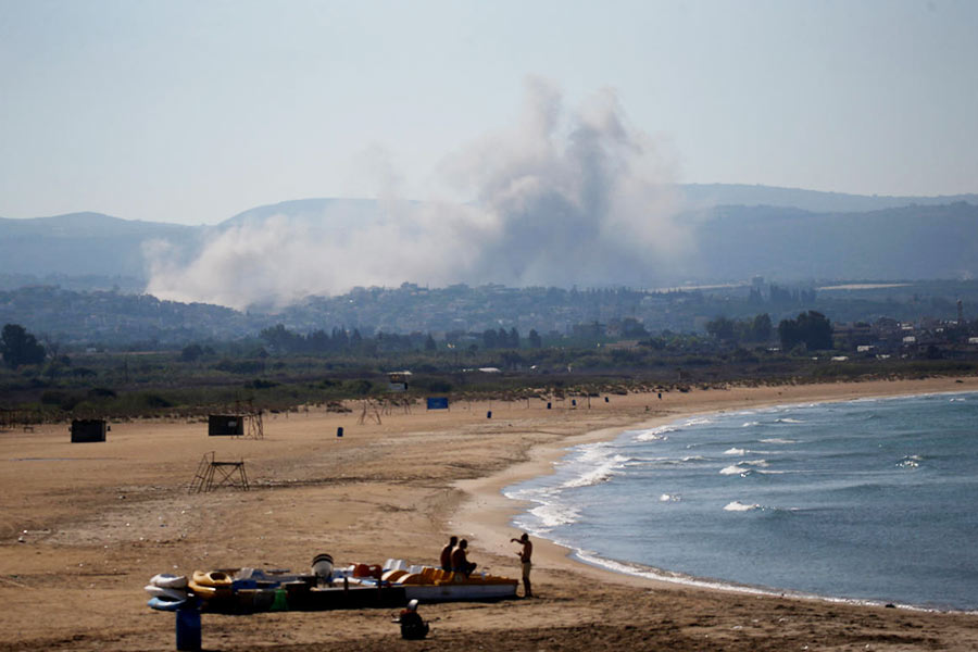 People spend time at a beach as smoke billows in the background over southern Lebanon following an Israeli strike, amid ongoing cross-border hostilities between Hezbollah and Israeli forces, as seen from Tyre, Lebanon September 26, 2024. 
