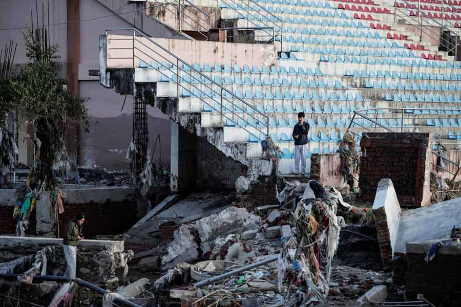 A woman walks past a damaged road next to a partially collapsed football stadium as the floodwater recedes in an area that was flooded by the overflowing Bagmati River following heavy rains, in Lalitpur.
