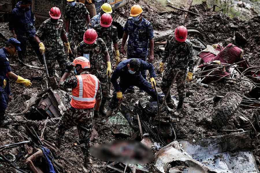 Rescue personnel work to retrieve a body recovered from a debris of a passenger bus after a landslide triggered by heavy rainfall struck passenger vehicles passing by the Tribhuwan Highway in Dhading.