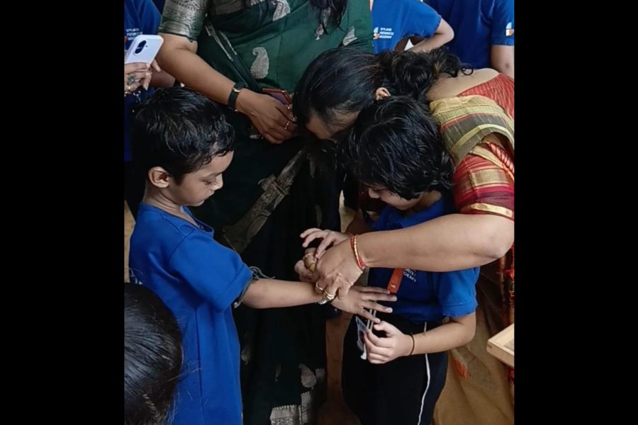 A JFA student ties a rakhi on the wrist of a Neev student