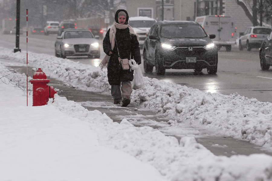 A pedestrian walks on a snow-covered sidewalk in Wheeling, Ill., Monday, Dec. 1, 2025.