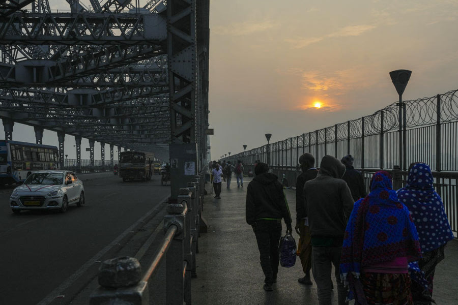 Pedestrians walk across Howrah Bridge on a winter morning as vehicles move alongside, in Kolkata.