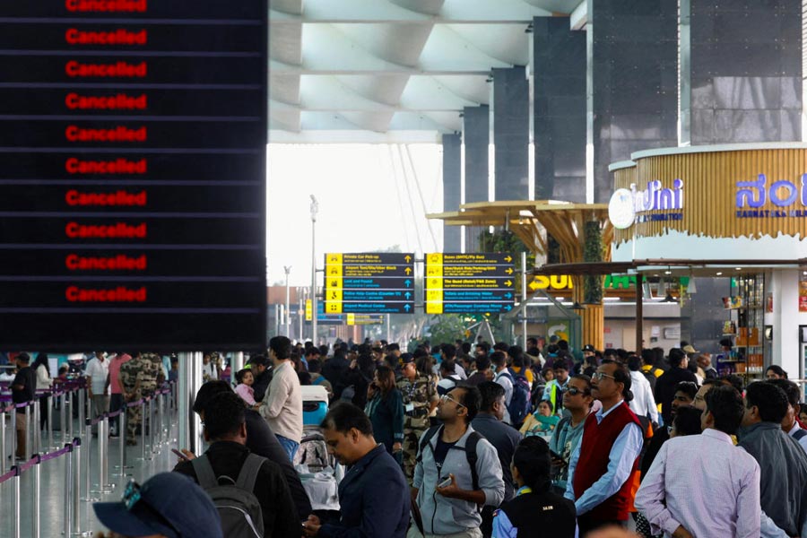 Travellers look at updates on flights, as they stand next to a screen displaying details of cancelled IndiGo airlines flights, at Kempegowda International Airport in Bengaluru, India, December 6, 2025.