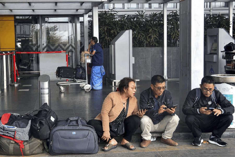 Passengers look at their mobile phones as they wait amid IndiGo flight disruptions, at Netaji Subhash Chandra Bose International Airport in Kolkata, Saturday, Dec. 6, 2025.