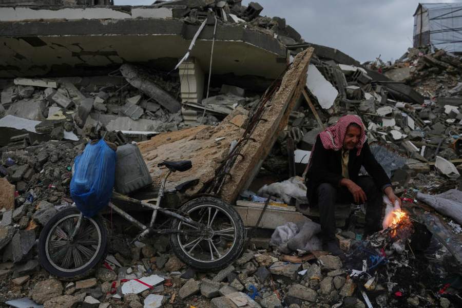 Palestinian Mohammed al-Jabri, 58, warms himself next to the fire as he sits on the rubble of a building destroyed during the Israeli air and ground operations in the Sheikh Radwan neighborhood, in Gaza City, Friday, Dec. 12, 2025.