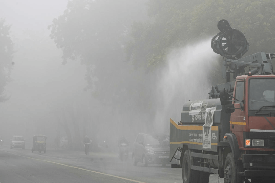 A municipal truck sprays water on a roadside to suppress dust and pollution amid dense foggy conditions, in New Delhi, Monday, Dec. 15, 2025.