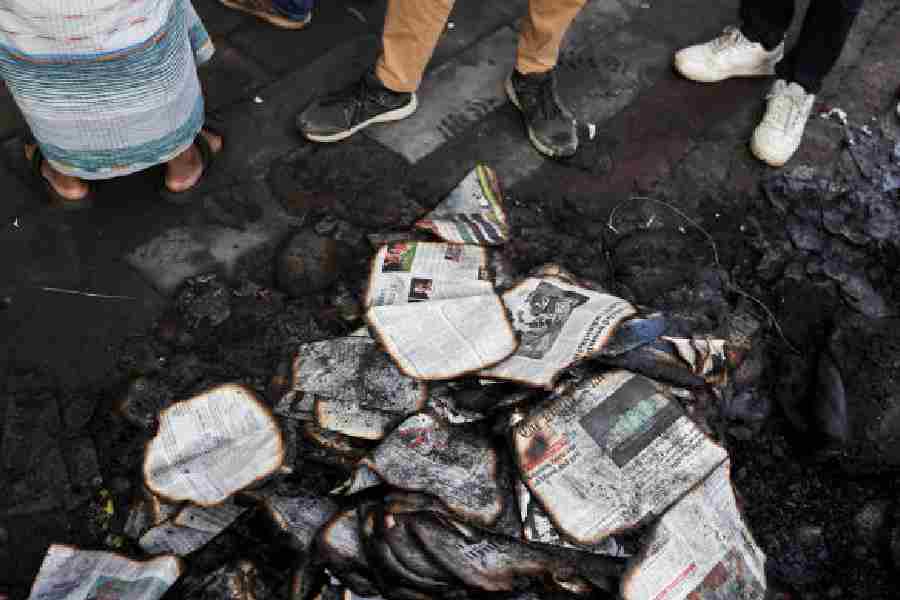 People stand next to burnt newspapers in front of the Daily Star building following the death of Sharif Osman Hadi, in Dhaka