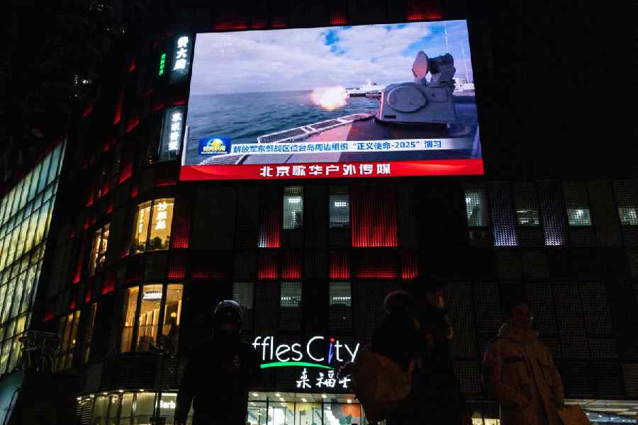 People walk by a giant screen during a broadcast of news on China's military drills around Taiwan, in Beijing, China, December 29, 2025.