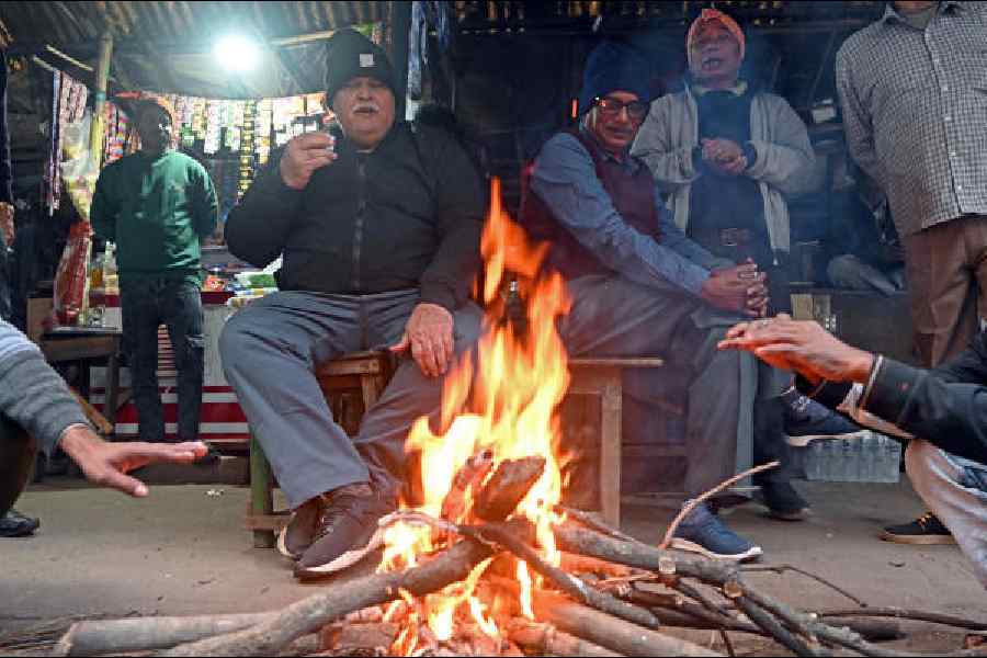 Visitors to a tea stall in the Esplanade area warm themselves around a fire on Monday afternoon
