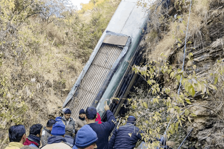 People gather around a damaged bus which fell-off a deep gorge, in Almora district, Uttarakhand, Tuesday, Dec. 30, 2025.