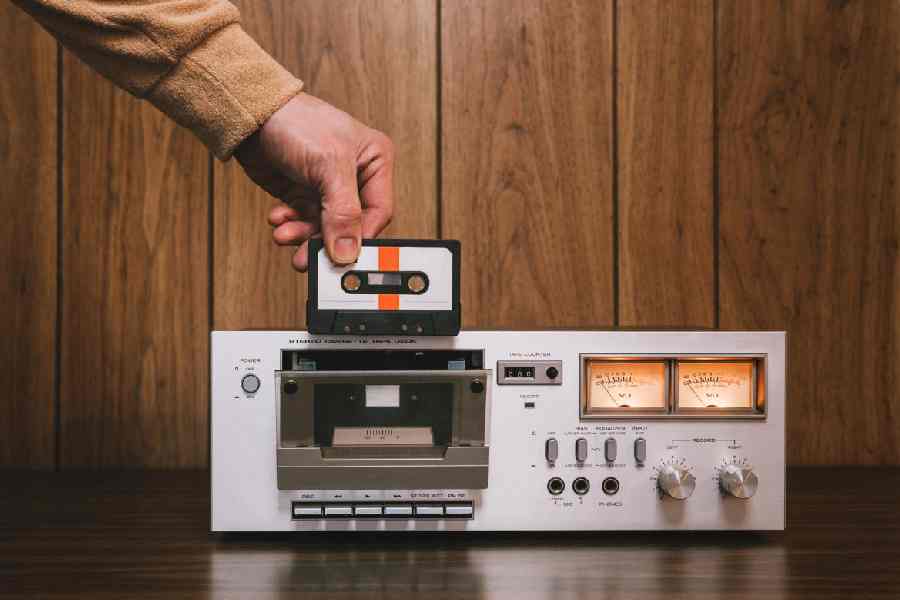 A vintage looking tape player recorder stereo sits on the counter of a 1970's - 1980's living room with wood paneling