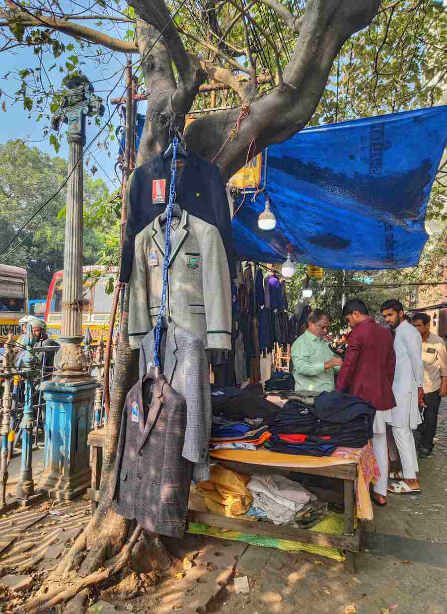 A hawker hangs an array of blazers from a tree on a pavement in BBD Bagh 
