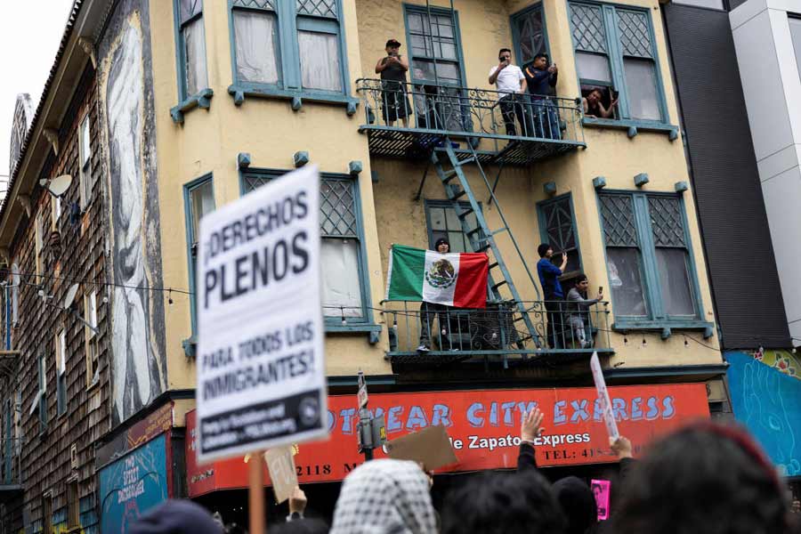 A man holds a Mexican flag from the fire escape of an apartment building in the Mission District during a protest against federal immigration sweeps, in San Francisco, California, U.S.