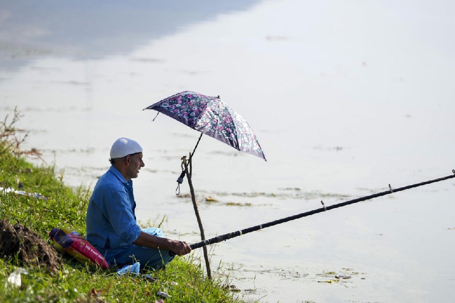 A man uses an umbrella for protection from the scorching sun while catching fish on a hot summer day, at Dal Lake in Srinagar