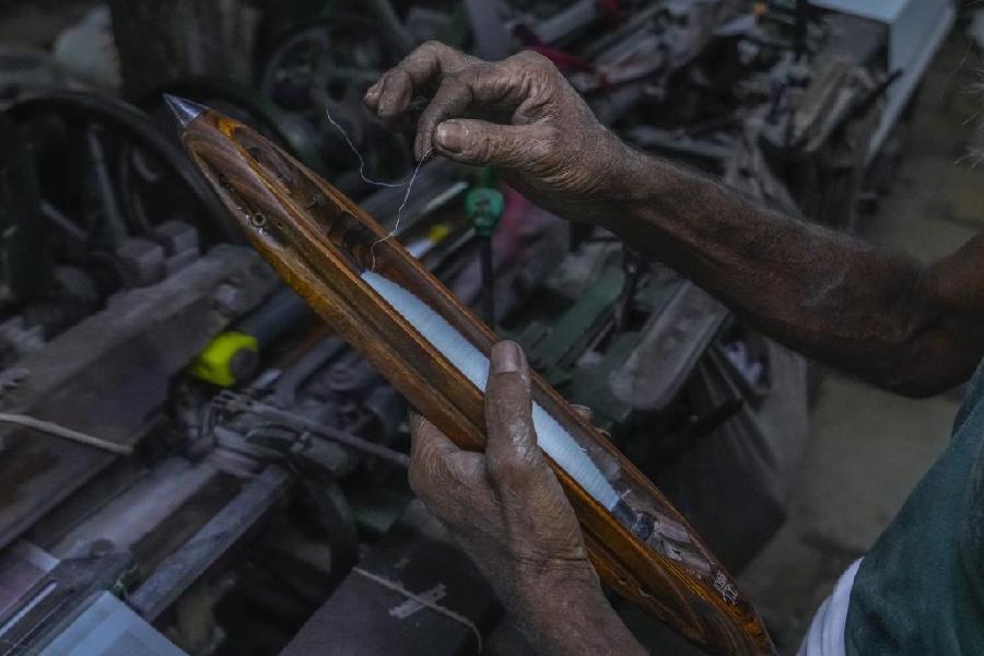 A weaver pulls a length of thread from a shuttle before feeding it to a power weaving loom