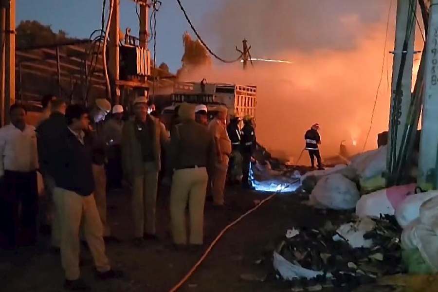 Police personnel and others gather as firemen try to douse a fire breaking out in a cluster of huts near Rithala metro station at Rohini area, in New Delhi