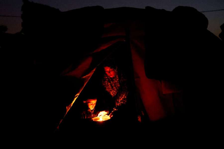 Displaced Palestinian Hanan al-Joujou sits with her child at the entrance of their tent, during a power cut, in Nuseirat, central Gaza Strip