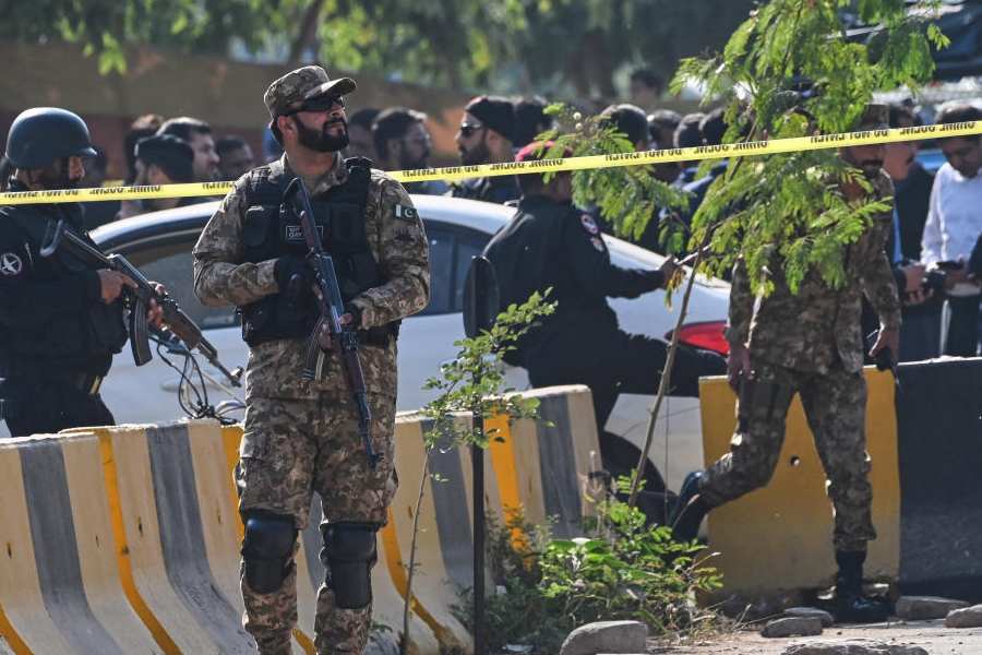 Pakistan's army soldiers and police officers stand guard while investigators examine a damage car at the site of a suicide bombing outside the gates of a district court, in Islamabad, Pakistan, Tuesday, Nov. 11, 2025.