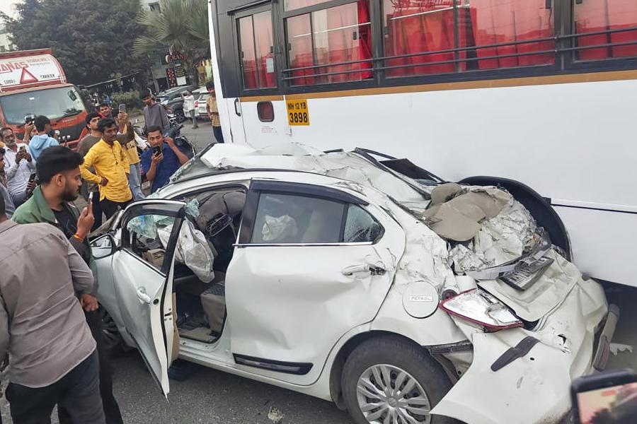 People stand near mangled remains of a car after an accident on the Mumbai-Bengaluru Highway, in Pune, Maharashtra, Thursday, Nov. 13, 2025.