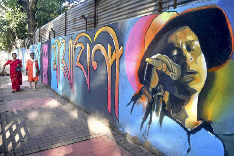Women walk past a mural of late singer Zubeen Garg painted on a roadside wall in Guwahati, Assam. 