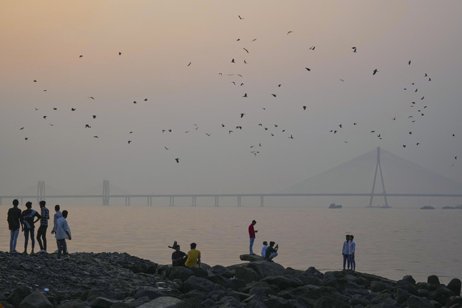 People sit along the shoreline at Dadar Beach as the Bandra-Worli Sea Link remains shrouded in smog, in Mumbai, Thursday, Nov. 27, 2025.