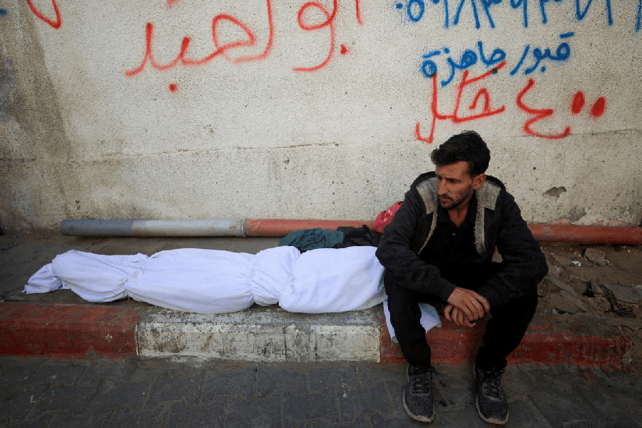 A mourner sits next to the body of a Palestinian who, according to medics, was killed in overnight Israeli strikes, at Al-Shifa Hospital in Gaza City, November 20, 2025.