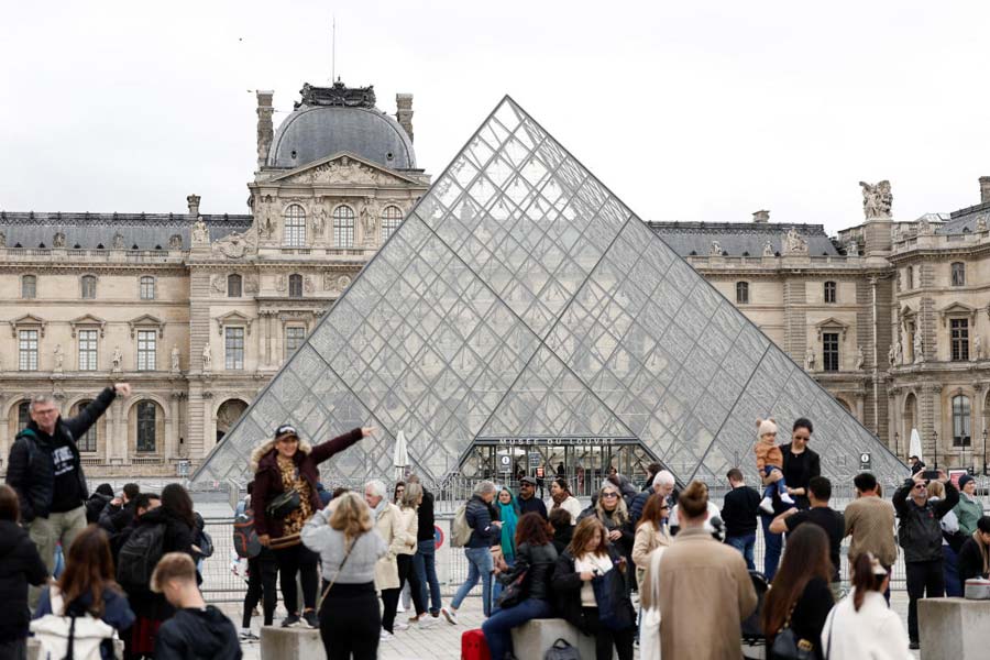 People stand near the glass Pyramid of the Louvre Museum.