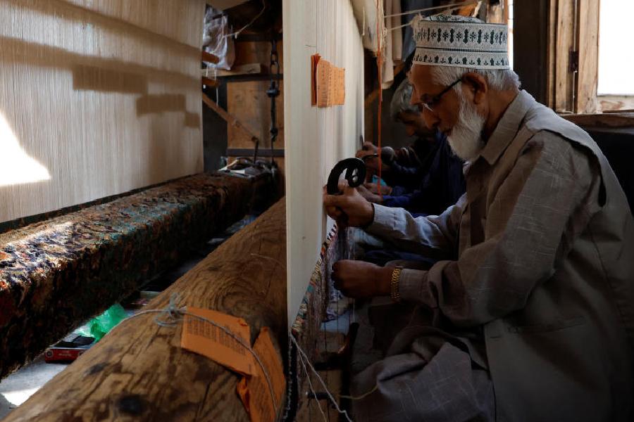 Ghulam Qadir, 75, an artisan, weaves a Kashmiri hand-knotted carpet along with other artisans inside a workshop in Srinagar