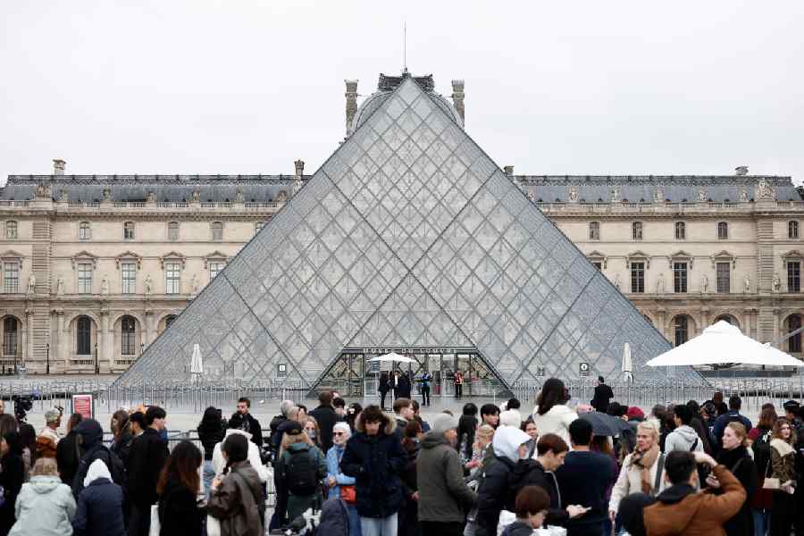 People stand near the glass Pyramid of the Louvre Museum as the museum remains closed the day after a spectacular jewel heist by thieves who broke into the landmark by using a crane and smashing an upstairs window, stealing priceless jewelry from an area that houses the French crown jewels before escaping on motorbikes, in Paris, France, October 20, 2025.