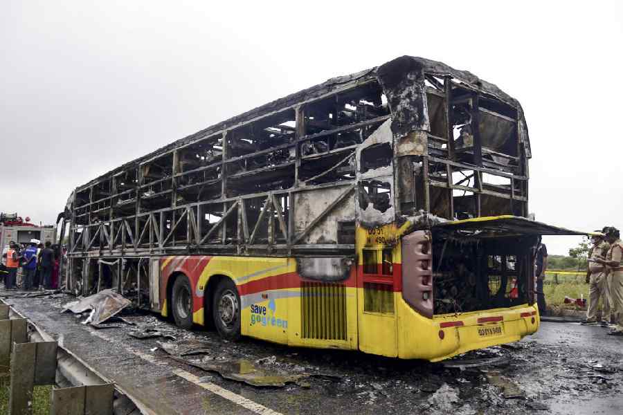 Police personnel investigate the spot where a Bengaluru-bound private bus caught fire after colliding with a two-wheeler, with the blaze being triggered after the motor bike with its fuel cap open was dragged underneath the bus, in Kurnool district, Andhra Pradesh, Friday, Oct. 24, 2025.