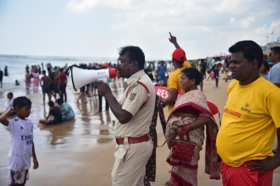 A fire brigade officer uses a loudhailer to alert people about Cyclone Montha at the crowded Puri beach on Sunday