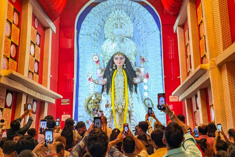Devotees capture the serene idol of Maa Jagadhatri, glowing in white and gold against the red backdrop