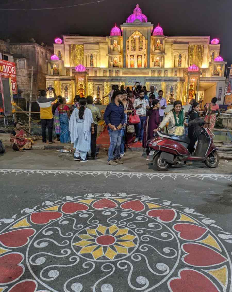 A rangoli-inspired road painting leads to a palace-themed pandal illuminated in soft gold and pink domes