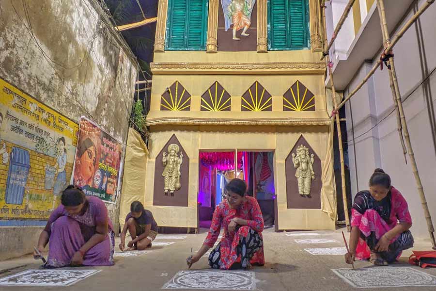 Women artists adorn the street with intricate alpana designs, adding a touch of tradition to the pandal entrance