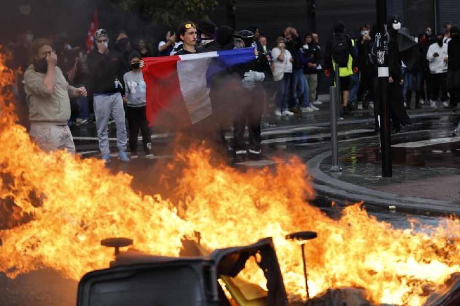 A protester of the "Block Everything" movement displays a French national flag next to burning cabbage bins in Lille, northern France, Wednesday, Sept. 10, 2025.