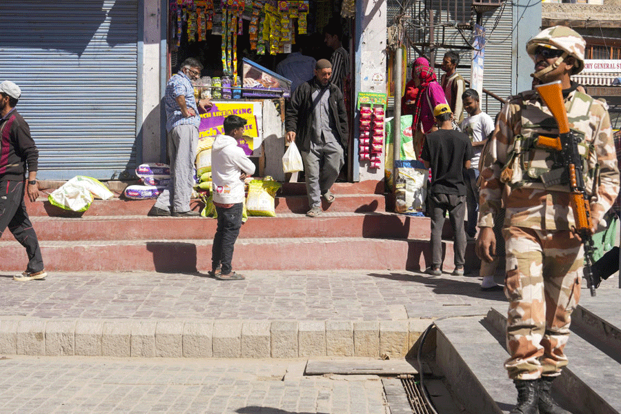People buy essentials as a security official keeps vigil after curfew restrictions were relaxed for two hours, in Leh, Ladakh, Saturday, Sept. 27, 2025.