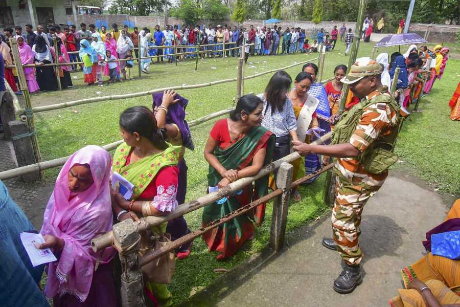 A security personnel assists voters as they wait in a queue before casting their votes in the Assam Assembly elections, at a polling station in Nagaon, Thursday, April 9, 2026.
