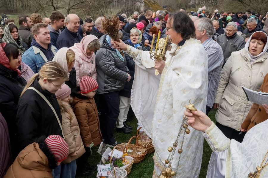 A priest blesses by sprinkling holy water during an Orthodox Easter service, following a 32‑hour ceasefire declared by Russia, amid Russia's attack on Ukraine, near the church at the National Museum of Folk Architecture in Kyiv, Ukraine April 12, 2026.