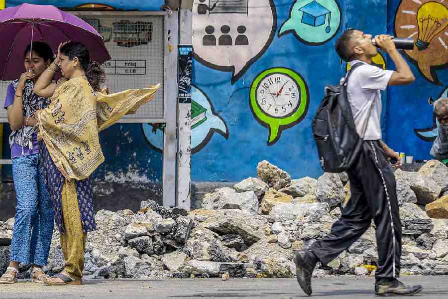 People use an umbrella and drink water to cope with the heat on a summer day in Hyderabad, Saturday, April 11, 2026.