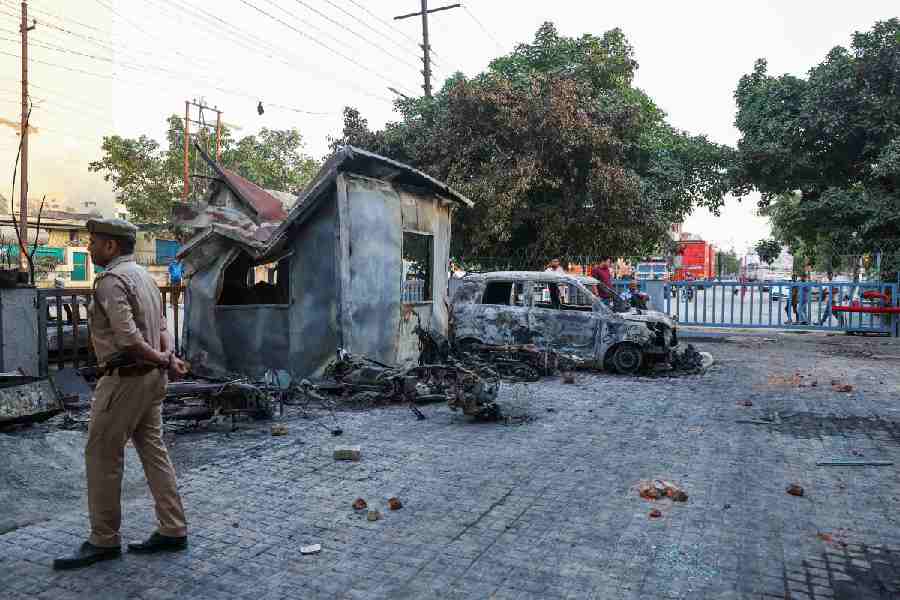 A police officer walks past a burnt vehicle during a workers' protest, after factory workers demanded a wage hike, amid soaring living costs due to disruptions caused by the U.S.-Israeli conflict with Iran, in Noida, India's industrial hub town in the state of Uttar Pradesh, India, April 13, 2026.