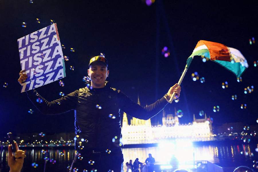 A man waves a flag and holds a poster as people celebrate following partial results on the day of the Hungarian Parliamentary election in Budapest, Hungary, April 13, 2026.   