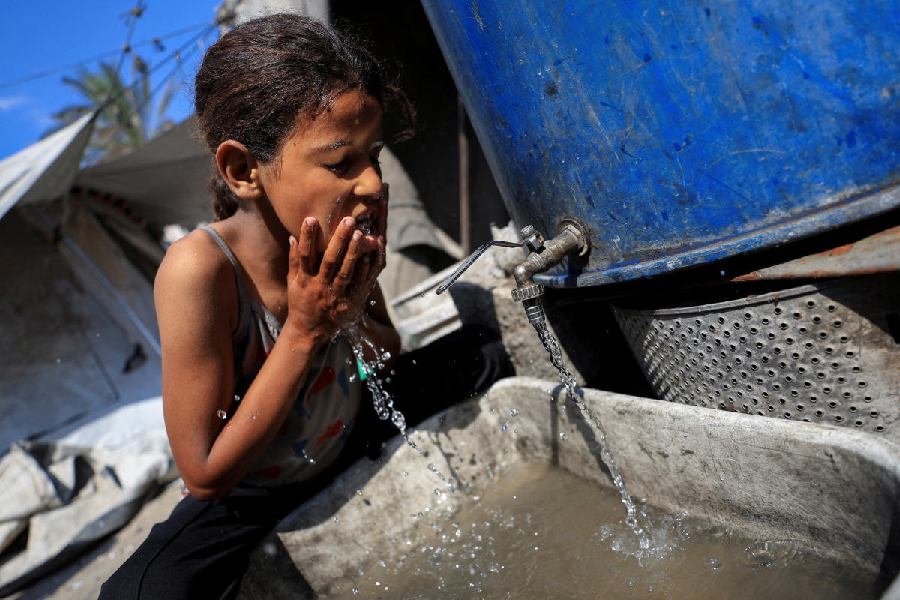 The daughter of displaced Palestinian man Akram Al-Manasra washes her face amid water shortages, outside their tent in Gaza City