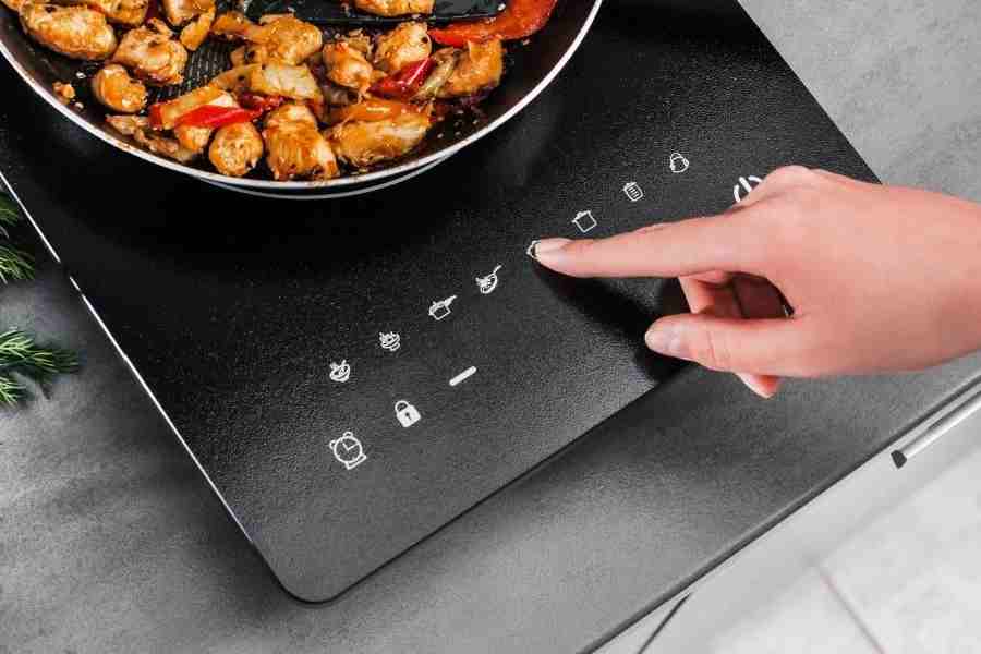A person\'s finger on a button on an induction cooktop.