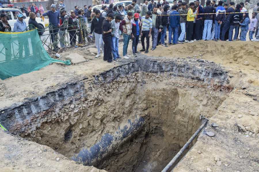 People gather near a 15-foot-deep pit dug for sewage work by the Delhi Jal Board (DJB), where a motorcyclist died after falling, at Janakpuri area, in New Delhi, Friday