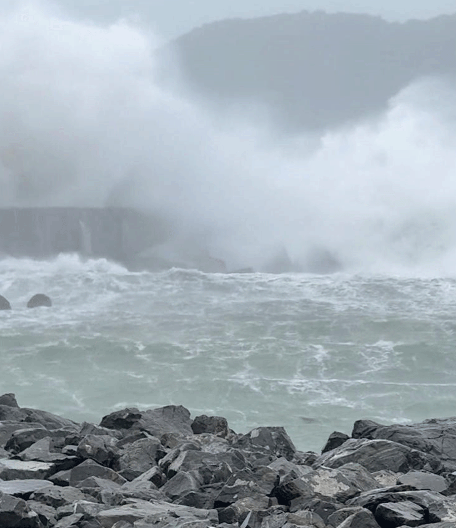 A large wave breaks over the breakwater at Lyall Bay