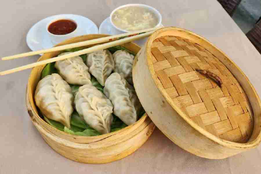 Steamed Chicken Momos served in a bamboo steamer basket with thick chicken soup and tangy momo sauce.