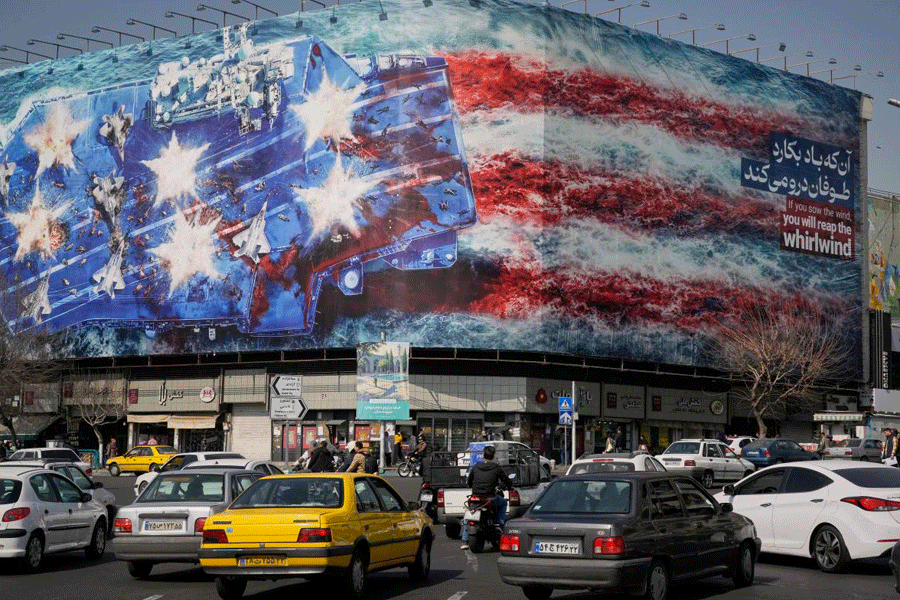 Vehicles pass a billboard depicting a U.S. aircraft carrier with damaged fighter jets on its deck and a sign in Farsi and English reading, "If you sow the wind, you'll reap the whirlwind," at Enqelab-e-Eslami (Islamic Revolution) Square in Tehran, Iran, Sunday, Feb. 22, 2026.