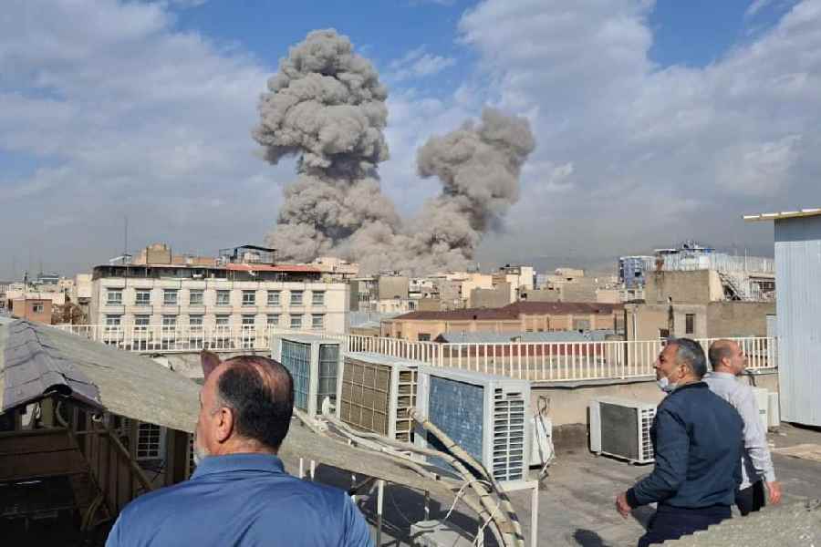 People watch as smoke rises on the skyline after an explosion in Tehran, Iran
