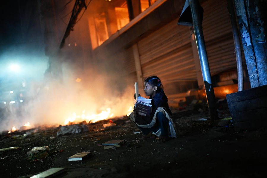 A girl rescues books from a shop near the premises of the Prothom Alo daily newspaper which was set on fire by angry protesters after news reached the country from Singapore of the death of a prominent activist Sharif Osman Hadi, in Dhaka, Bangladesh, Friday, Dec. 19, 2025.