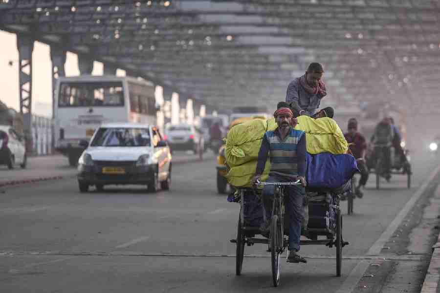 A cycle rickshaw loaded with goods moves across the Howrah Bridge amid traffic, on a winter morning, in Kolkata, Monday, Jan. 12, 2026.